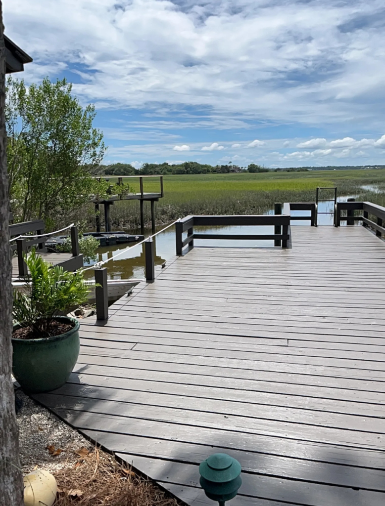 Large gray refinished wood deck with dark railings extending toward a waterfront marsh and dock.