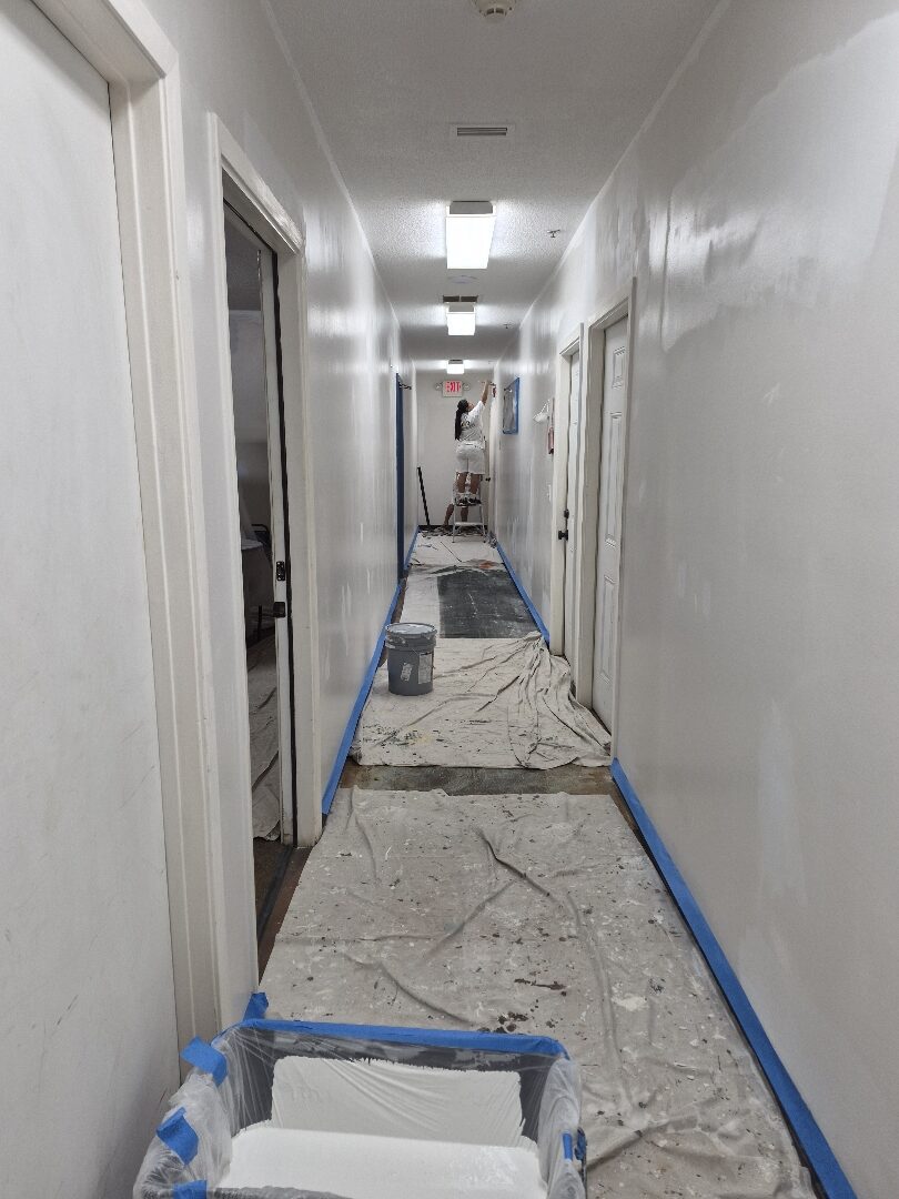 Commercial hallway being professionally repainted with floors protected by drop cloths and trim masked for painting.