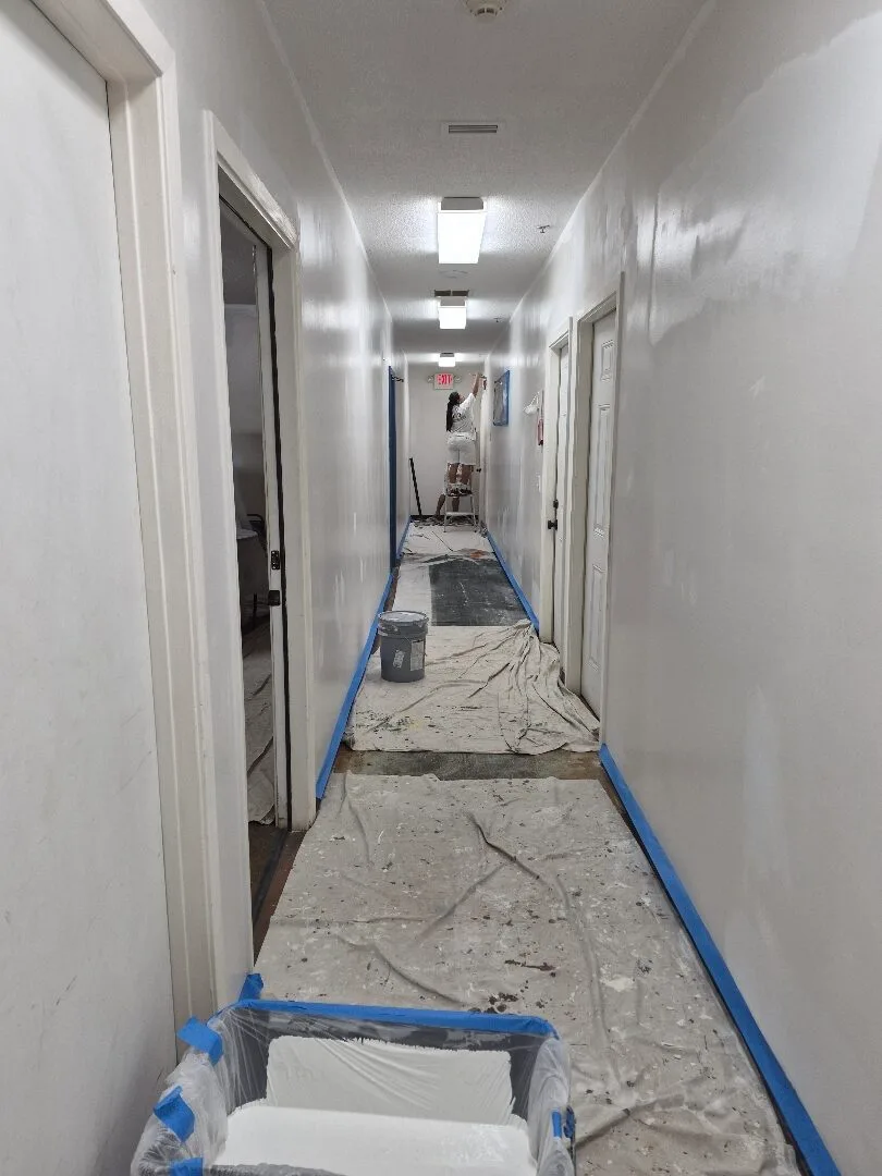 Commercial hallway being professionally repainted with floors protected by drop cloths and trim masked for painting.