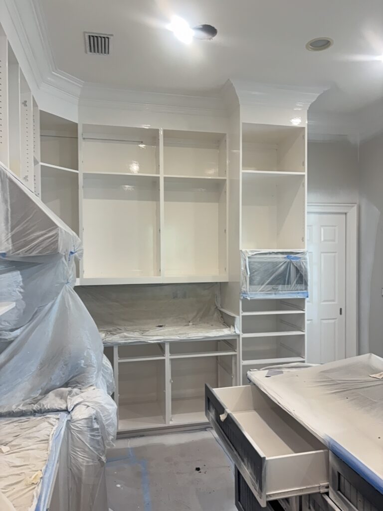 Kitchen cabinets being professionally painted and refinished in St. Simons Island, GA, with countertops and appliances protected during spraying.