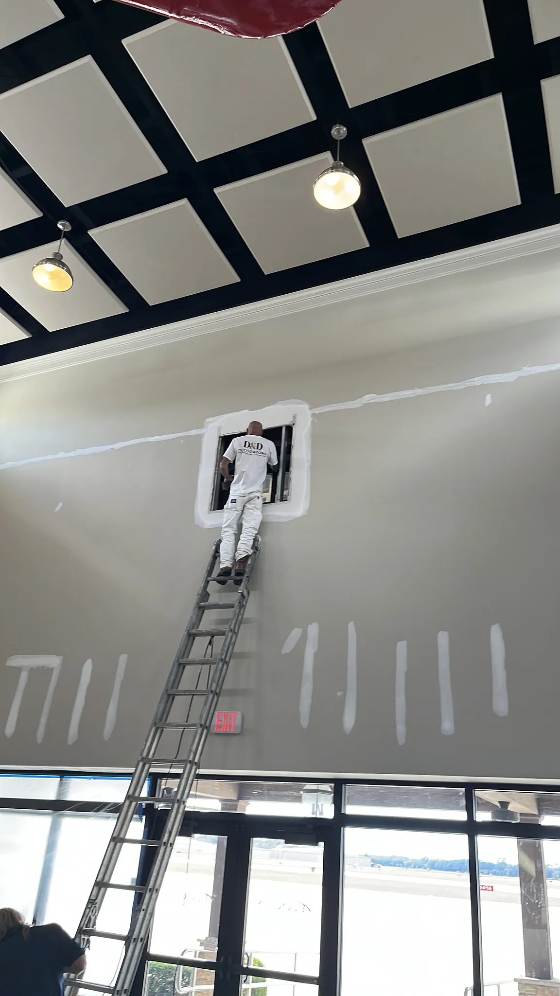 Commercial interior wall repair and painting in progress with a D&D Decorators painter working from a ladder.