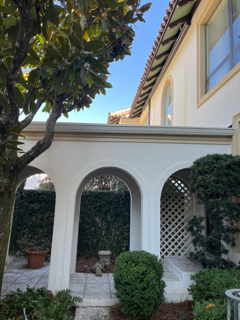 White stucco courtyard arches and exterior walls with landscaped garden areas at a residential home.