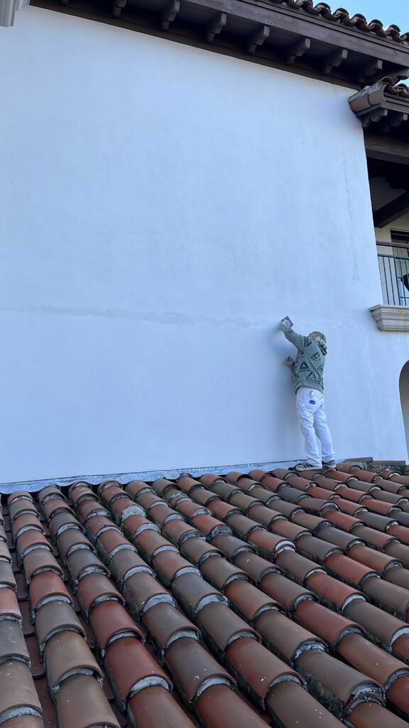 Professional stucco wall repair and surface preparation in progress on a large exterior home before repainting.