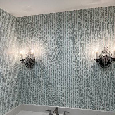 Patterned wallpaper installed on bathroom walls with decorative wall sconces and white trim.
