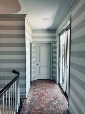 Striped wallpaper covering hallway and stairway walls with painted trim, brick flooring, and glass doors.
