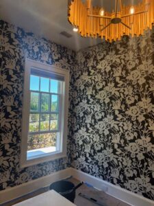Black wallpaper with oversized white floral pattern installed in a room with white trim and chandelier.
