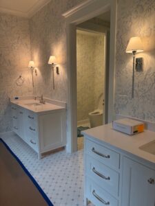 Light blue botanical wallpaper installed throughout a bathroom with white vanities and chrome sconces.