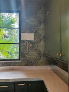 Dark botanical wallpaper installed around a window and green cabinetry with brass hardware.