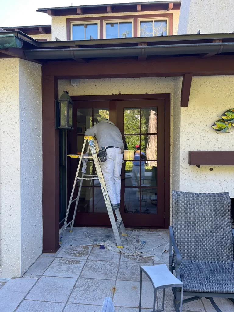 Painter refinishing dark brown exterior French doors with glass panes