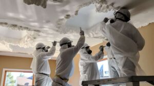 Painting crew removing popcorn ceiling texture while wearing protective equipment