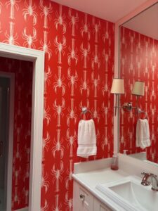 Bright red wallpaper with white lobster pattern installed in a bathroom above a white vanity.