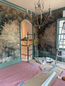 Scenic landscape mural wallpaper installed in a dining room with green trim and arched doorway.
