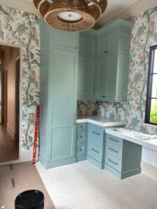 Tropical floral wallpaper installed around sage green built-in cabinetry and a black-framed window.