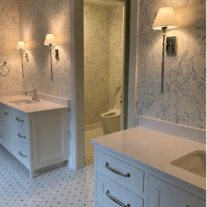 Blue and white toile wallpaper in a bathroom with white vanities and polished wall sconces.