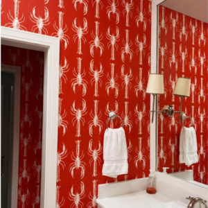Bright red lobster-pattern wallpaper in a powder room with white trim and polished wall sconces.