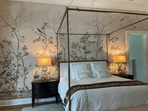 Chinoiserie wallpaper mural featuring flowering trees, birds, and butterflies behind a brass canopy bed in a St. Simons Island, GA bedroom.