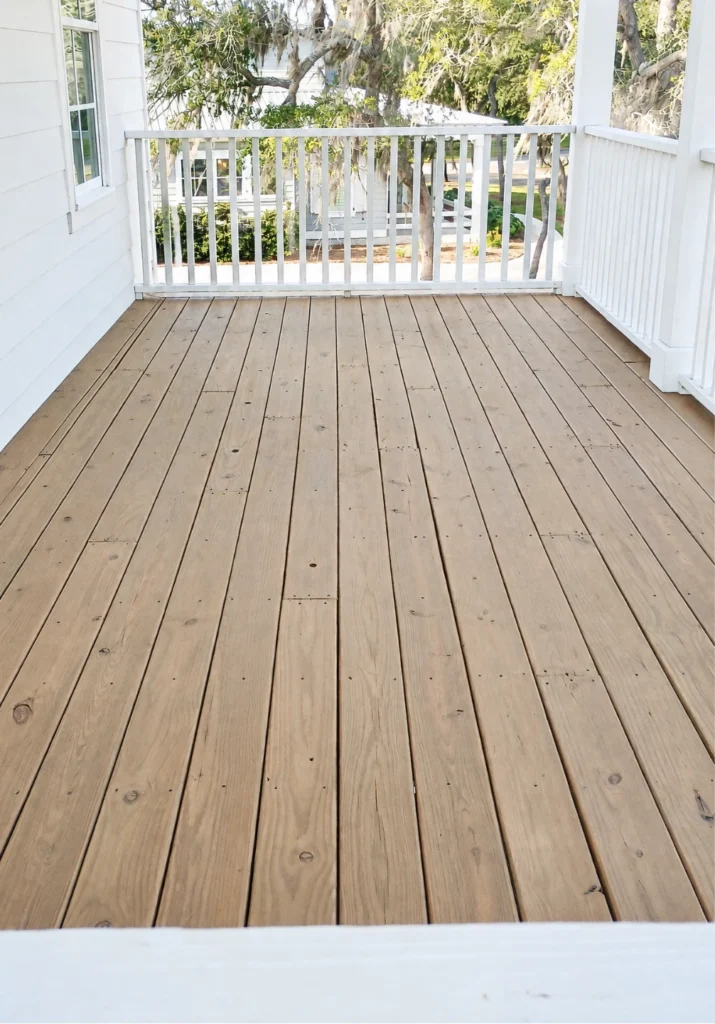 Natural wood deck flooring with a light brown finish, white-painted porch railings, and exterior siding on an elevated residential porch.