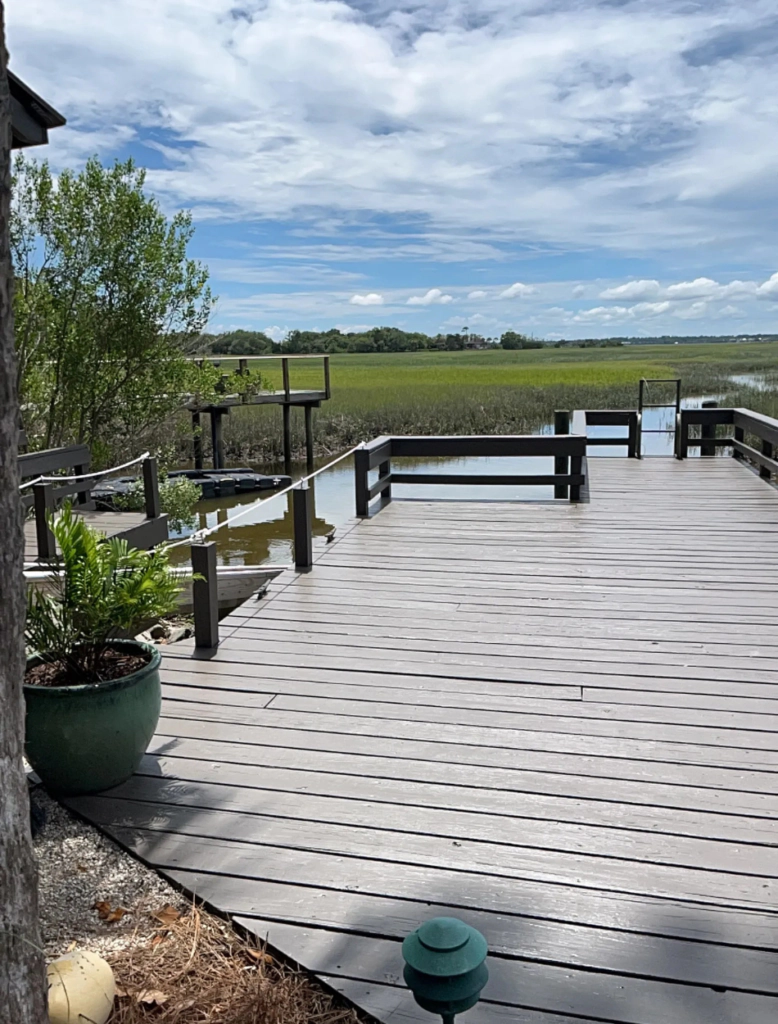 Large gray refinished wood deck with dark railings extending toward a waterfront marsh and dock.