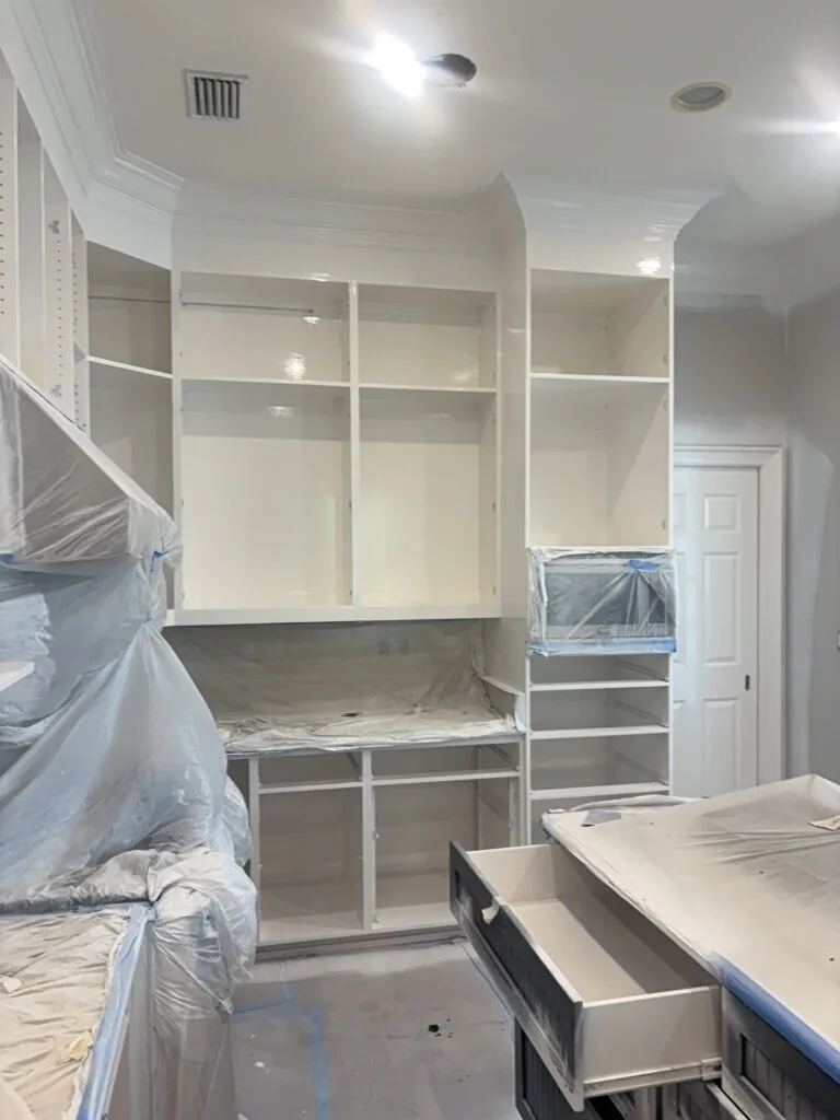 Kitchen cabinets being professionally painted and refinished in St. Simons Island, GA, with countertops and appliances protected during spraying.