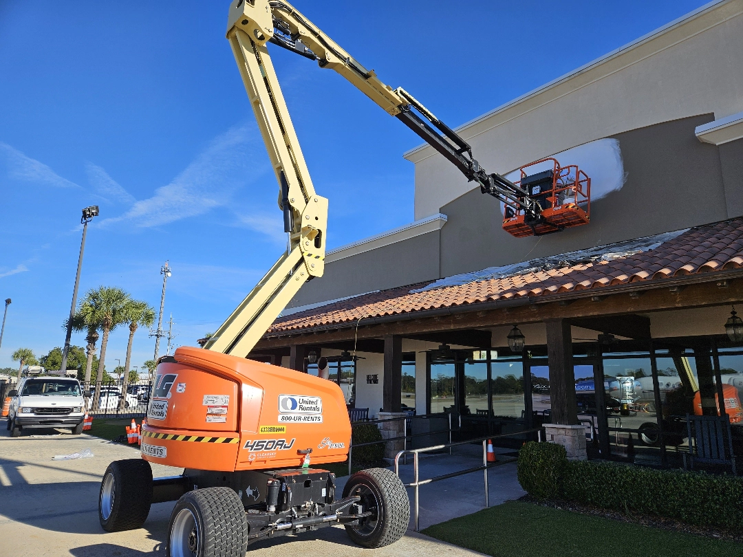 Commercial exterior painting in progress using a boom lift to repaint the upper walls of a large business building.