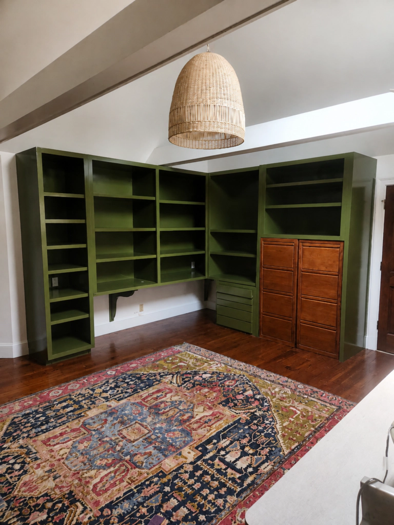 Custom built-in bookshelves and cabinetry professionally painted deep green, with natural wood cabinet doors and hardwood floors.