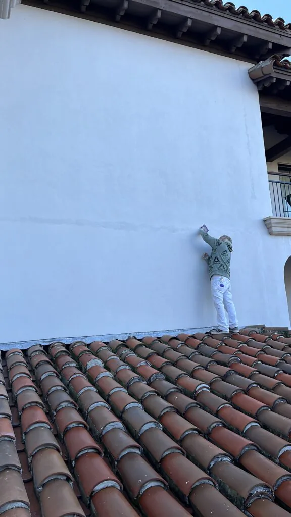 Professional stucco wall repair and surface preparation in progress on a large exterior home before repainting.