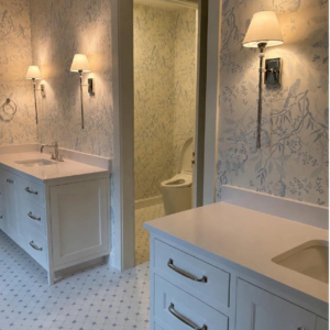 Blue and white toile wallpaper in a bathroom with white vanities and polished wall sconces.